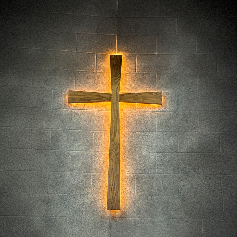 An image of a cross lit from behind on a gray brick wall